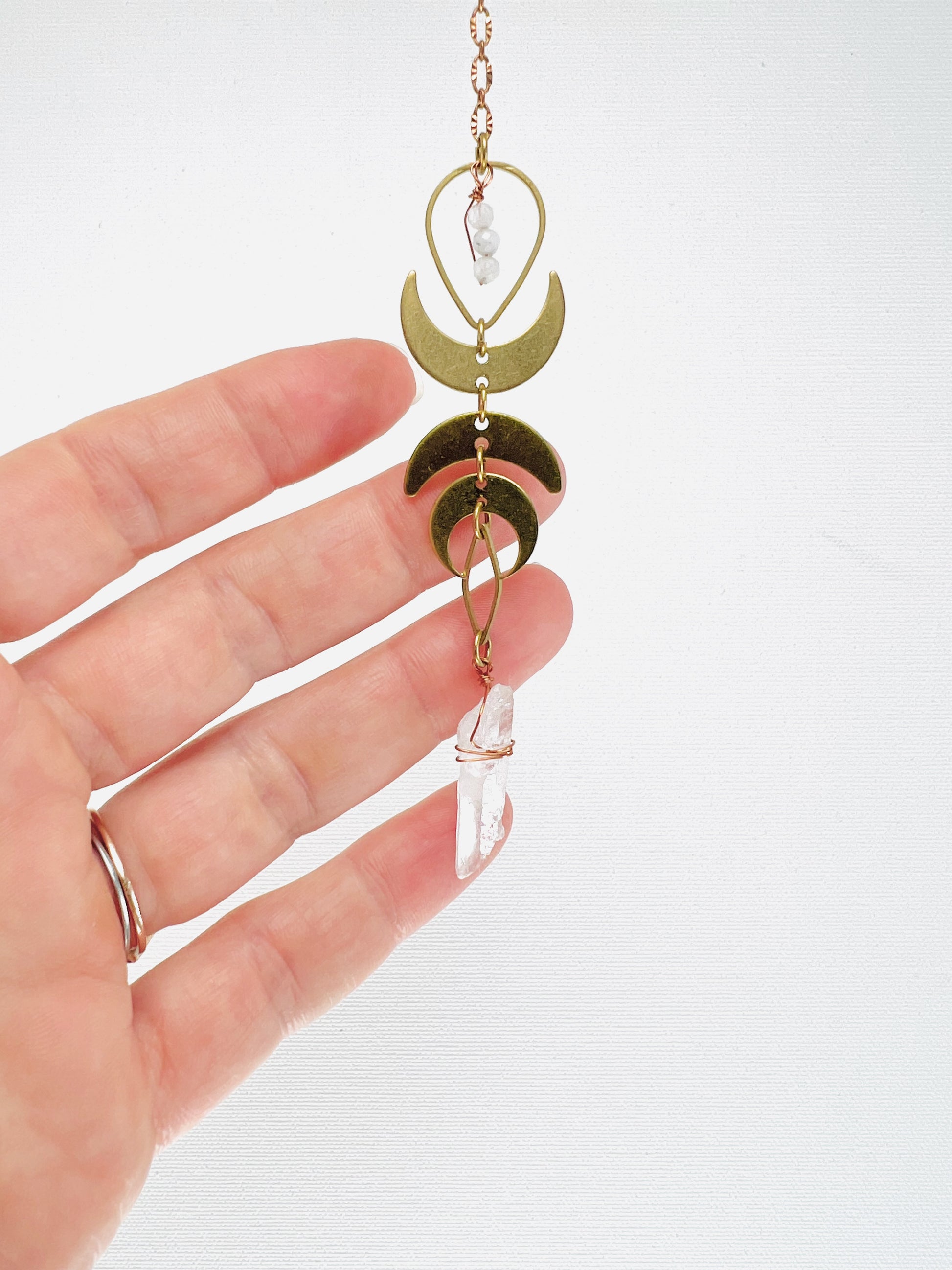 A pendulum A photo of three dimensional art, meant to hang on the wall. It is a combination of crystals, metals and wood and looks similar to a dream catcher. It helps to attract your best life, through the crystals meanings.there are also crescent moons and other brass charms on it.