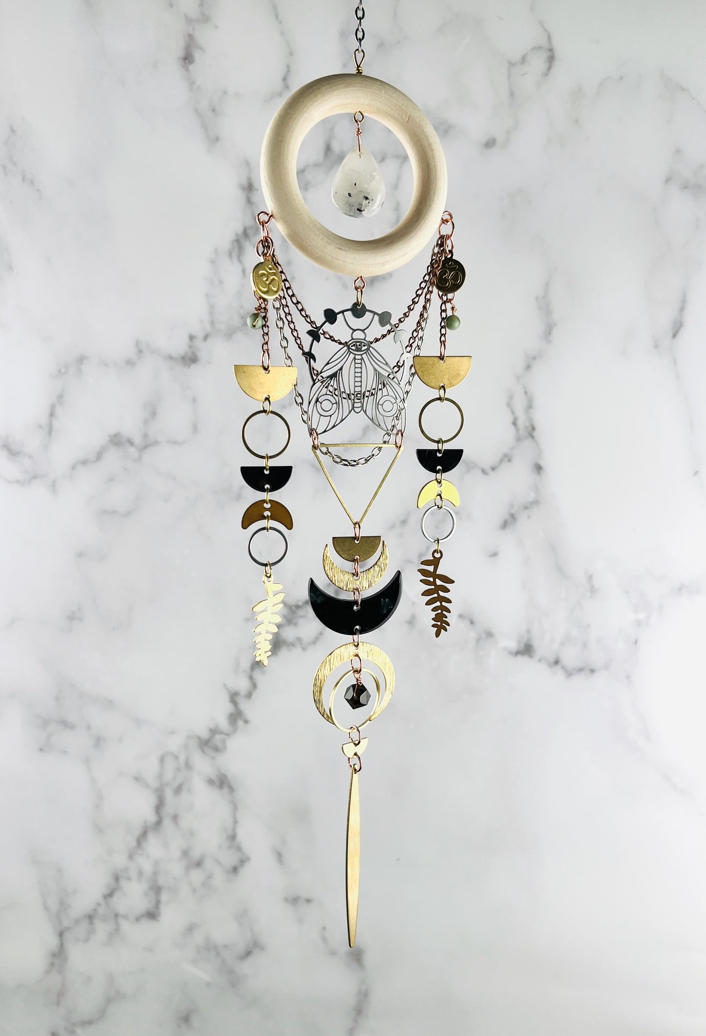 A photo of three dimensional art, meant to hang on the wall. It is a combination of crystals, metals and wood and looks similar to a dream catcher. It helps to attract your best life, through the crystals meanings.there are also crescent moons and other brass charms on it.