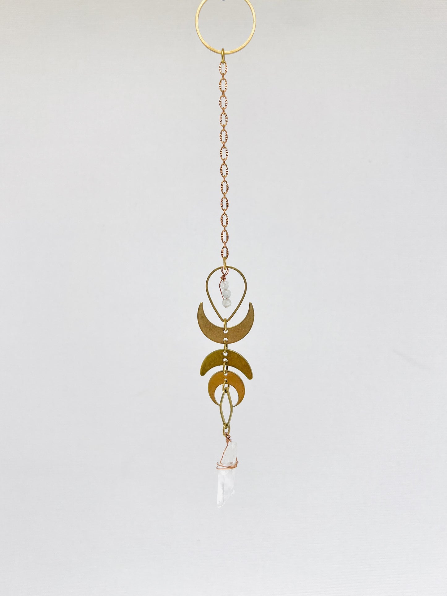 Pendulum hanging art A photo of three dimensional art, meant to hang on the wall. It is a combination of crystals, metals and wood and looks similar to a dream catcher. It helps to attract your best life, through the crystals meanings.there are also crescent moons and other brass charms on it.