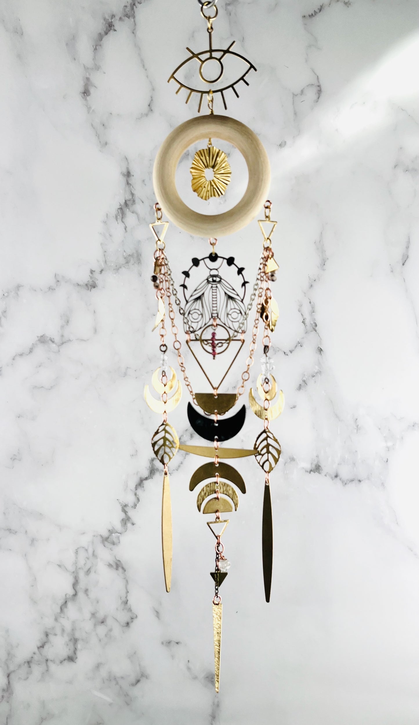 Labradorite, amazonite and prehnite manifestation charm crystal wall art for intuitive protection and emotional renewal. Decorative crystal wall hanging with geometric patterns on a marble background. shapes include wood ring, evil eye symbol, star burst, moon phase, moth, golden leaves, triangles, crescent moons, and circles