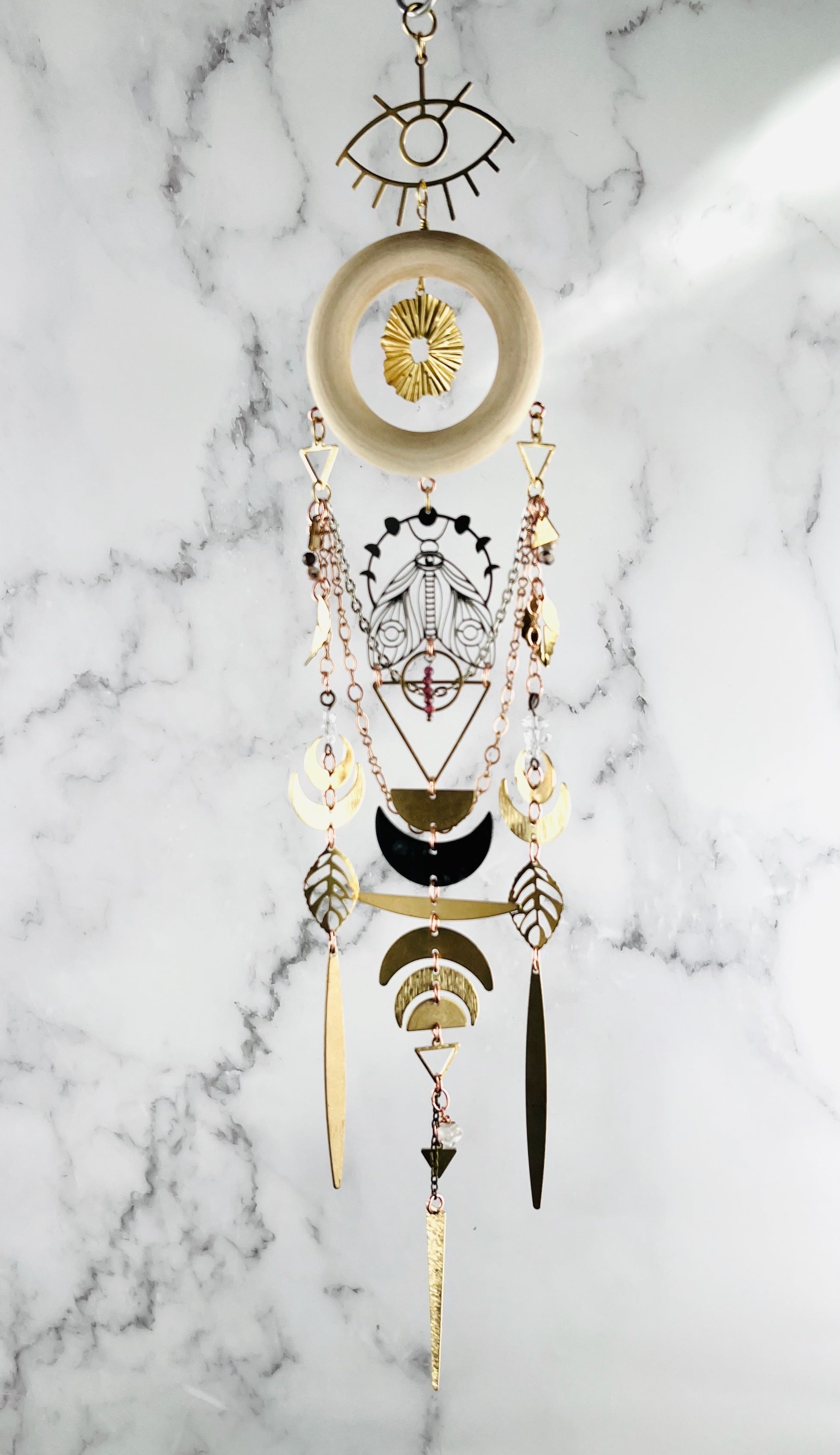 Labradorite, amazonite and prehnite manifestation charm crystal wall art for intuitive protection and emotional renewal. Decorative crystal wall hanging with geometric patterns on a marble background. shapes include wood ring, evil eye symbol, star burst, moon phase, moth, golden leaves, triangles, crescent moons, and circles