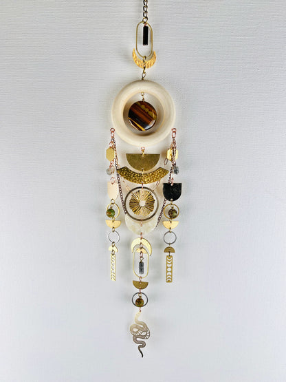 Decorative hanging crystal wall art with gold half circles, rings, ovals, moon phase, sun burst, crescent moons, hexagons, chain, silver rings, copper rings and wood ring, also snake and beads on a white background