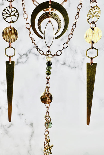 Metal components including copper colored chain, crescent moons, long triangles, tree of life, circle connectors and hexagon rings with wire wrapped beads, and star at the bottom all hanging in front of a marble wall.