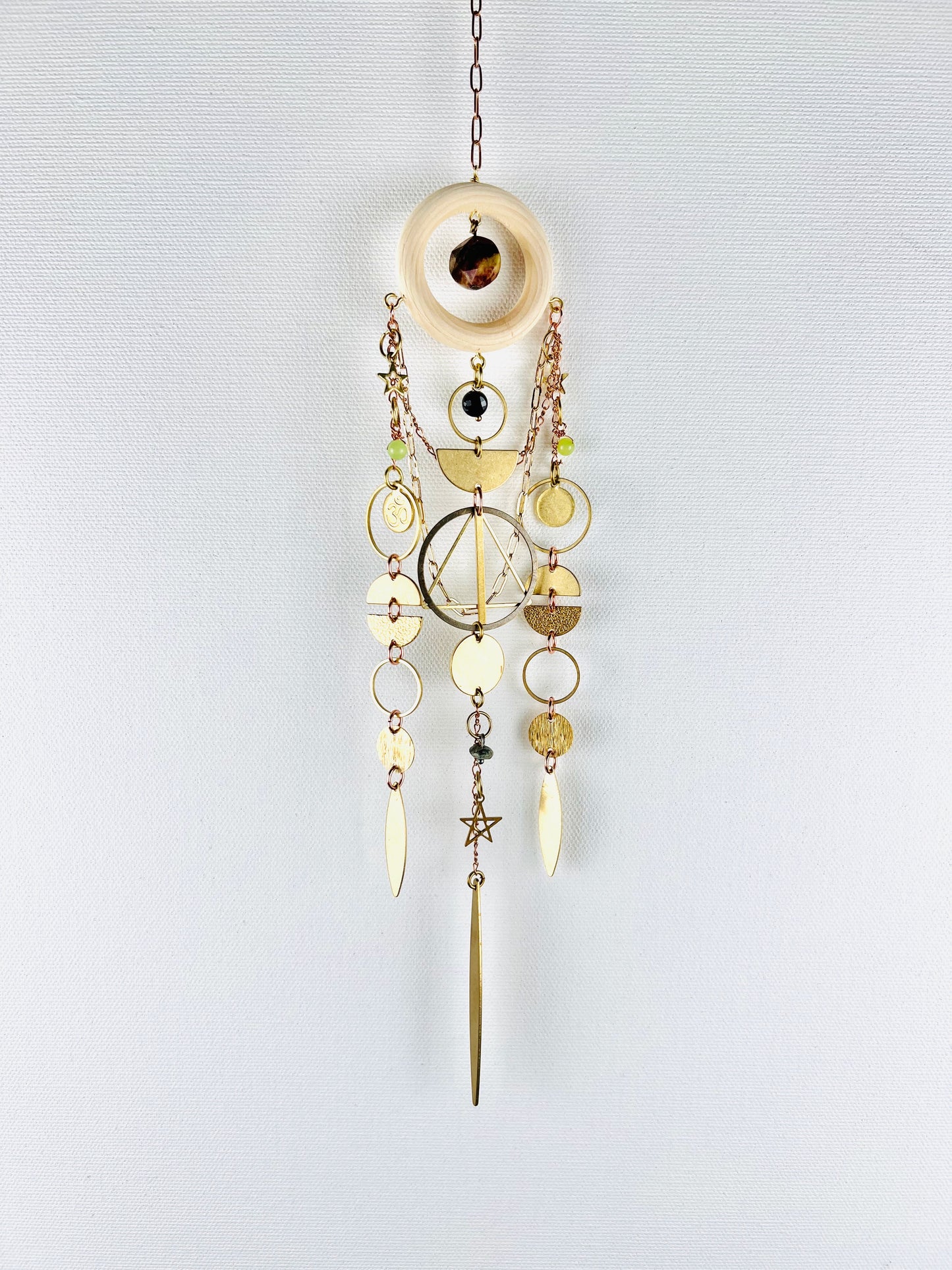 Decorative hanging ornament with gold and brass elements on a light gray background. Handmade Bloodstone, Onyx, Green Calcite, and Turquoise wall art manifestation charm created for intentional home decor.