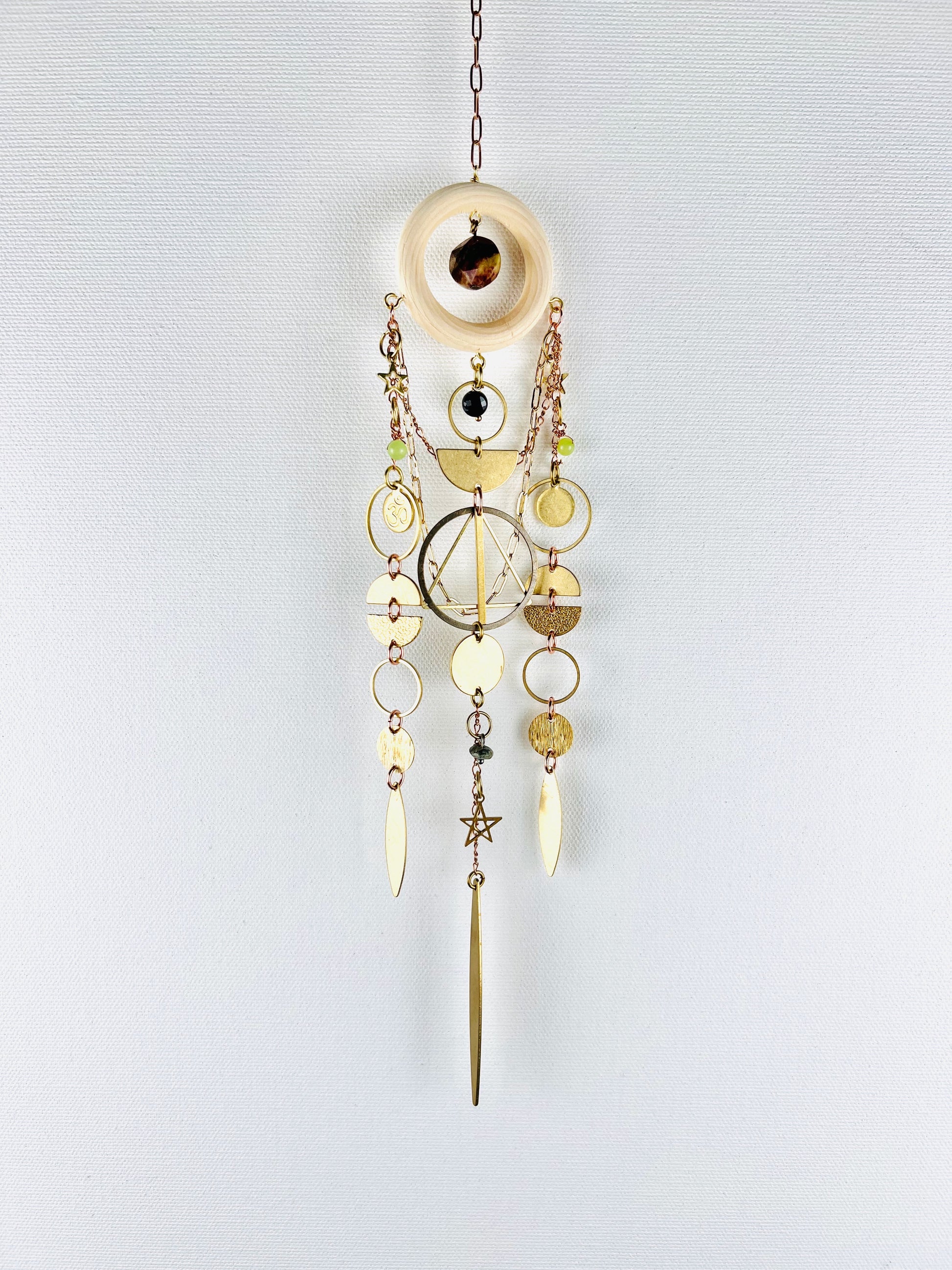 Decorative hanging ornament with gold and brass elements on a light gray background. Handmade Bloodstone, Onyx, Green Calcite, and Turquoise wall art manifestation charm created for intentional home decor.
