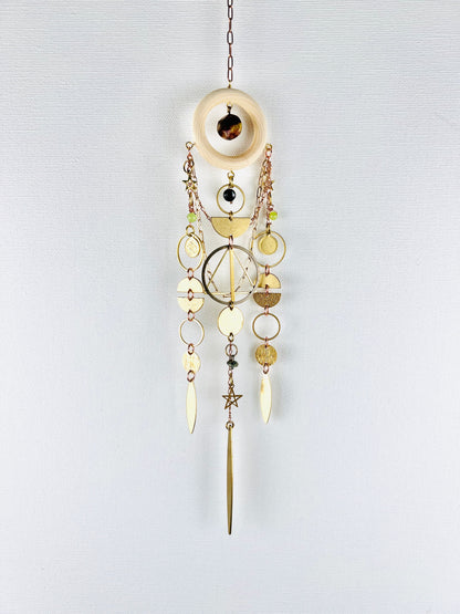 Decorative hanging ornament with gold and brass elements on a light gray background. Handmade Bloodstone, Onyx, Green Calcite, and Turquoise wall art manifestation charm created for intentional home decor.