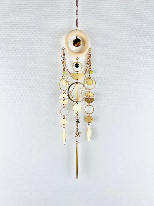 Decorative hanging ornament with gold and brass elements on a light gray background. Handmade Bloodstone, Onyx, Green Calcite, and Turquoise wall art manifestation charm created for intentional home decor.