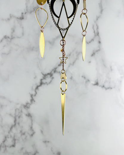 The bottom portion of a piece of crystal wall art depicted as three separate hanging metal patterns and a citrine bead with gold colored  shapes, including: upside down teardrops, diamonds, crescent moon, elongated eye shapes, triangles, half circles, rings, and a star.