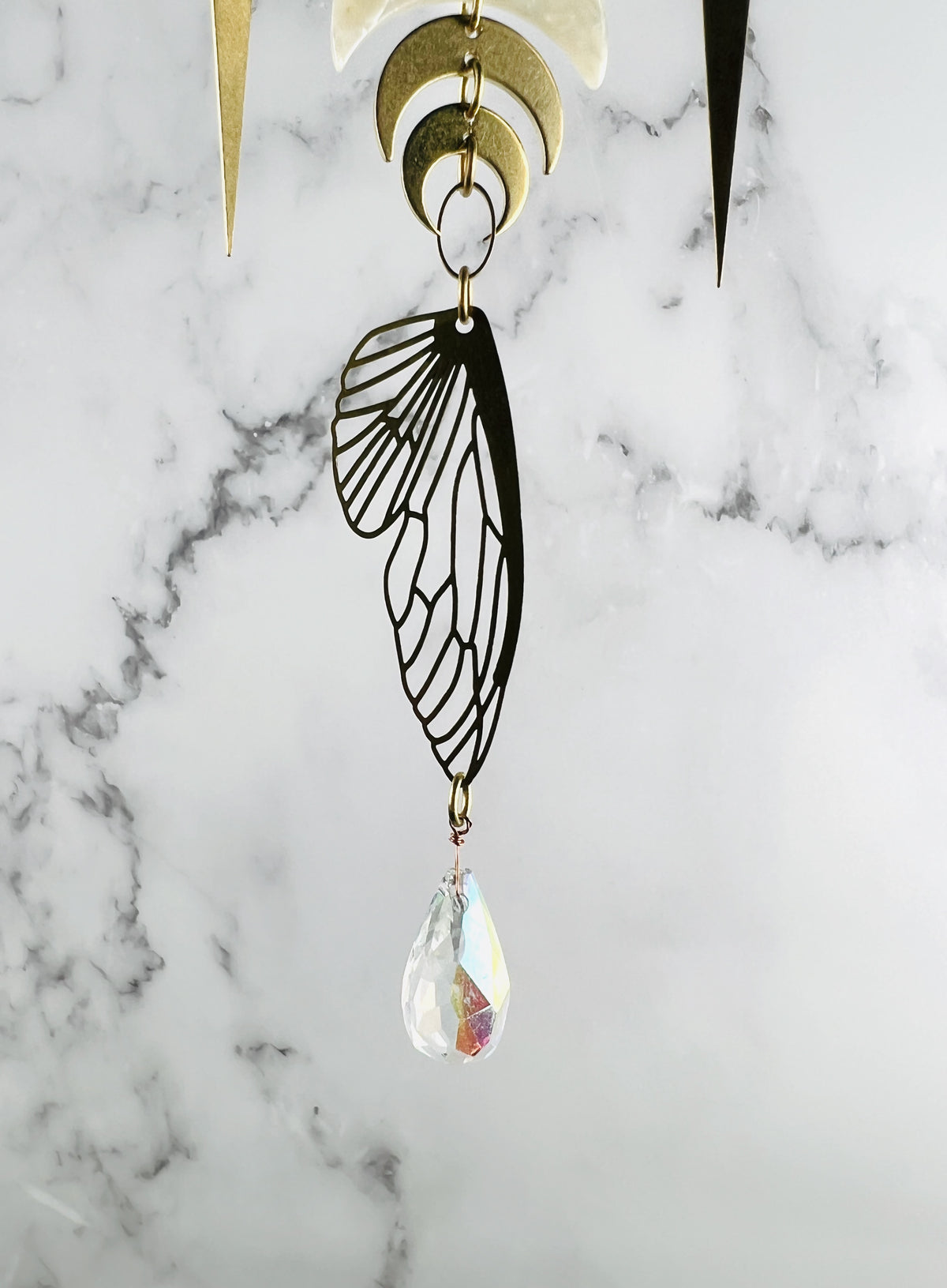Crescent moons and spikes with oval ring and bug wing with prism hanging from the bottom all in front of a marble wall.