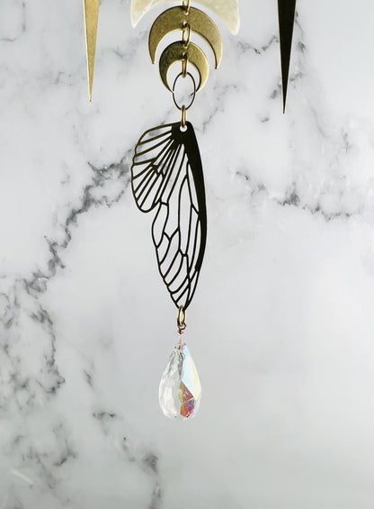 Crescent moons and spikes with oval ring and bug wing with prism hanging from the bottom all in front of a marble wall.