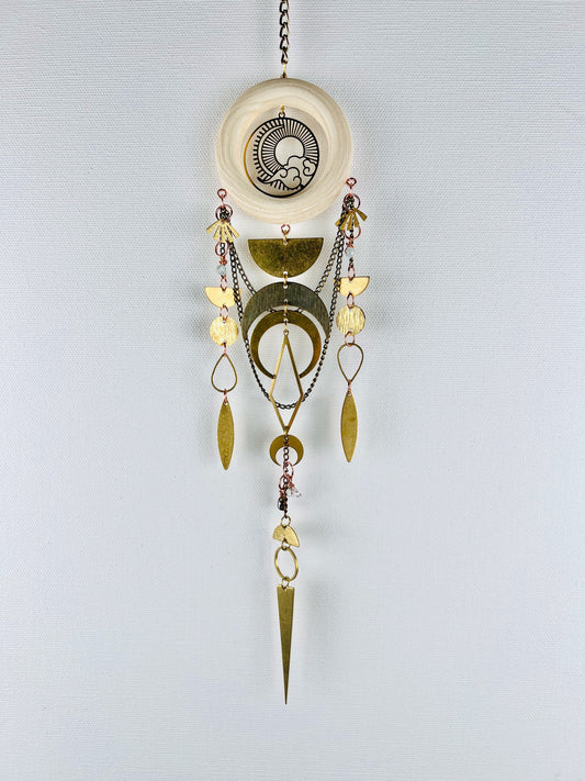 Decorative handmade hanging crystal wall art with gold and silver elements on a light gray background. Elements include Aquamarine, Green Tourmaline, Herkimer Diamonds, gold, colored, metal fans, half circle circles, crescent, moons, diamonds, oval, and along sharp triangle at the bottom.