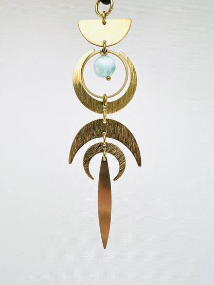 Gold and brass hanging ornament with a light blue gemstone on a white background. Handmade Green Moonstone manifestation mini charm used as a rearview mirror car charm and intentional home decor piece.