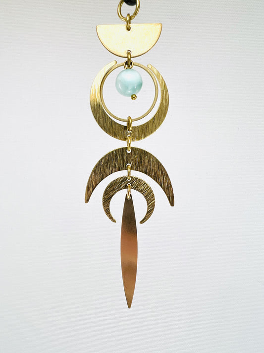 Gold and brass hanging ornament with a light blue gemstone on a white background. Handmade Green Moonstone manifestation mini charm used as a rearview mirror car charm and intentional home decor piece.