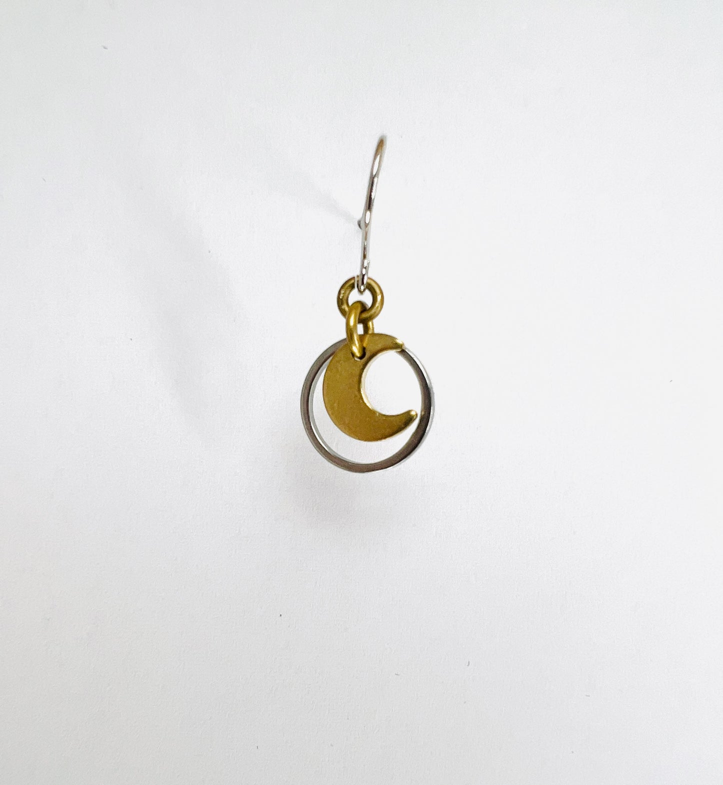 A single minimalist, dangle lightweight, gold-colored earring with a geometric silver circle and moon design, displayed against a white background.