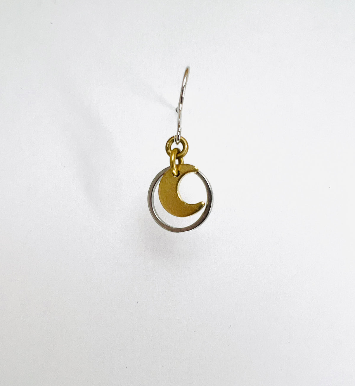 A single minimalist, dangle lightweight, gold-colored earring with a geometric silver circle and moon design, displayed against a white background.