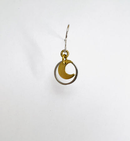 A single minimalist, dangle lightweight, gold-colored earring with a geometric silver circle and moon design, displayed against a white background.