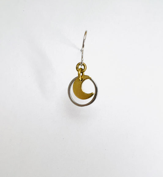 A single minimalist, dangle lightweight, gold-colored earring with a geometric silver circle and moon design, displayed against a white background.