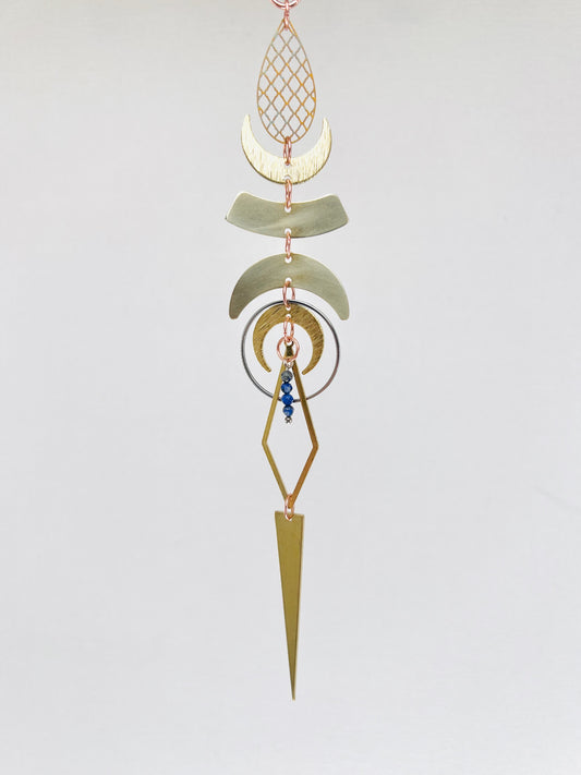 Decorative hanging gold and silver rearview mirror ornament with geometric shapes and royal blue beads on a light gray background. Handmade Lapis Lazuli manifestation mini charm used as a rearview mirror car charm and intentional home decor piece.