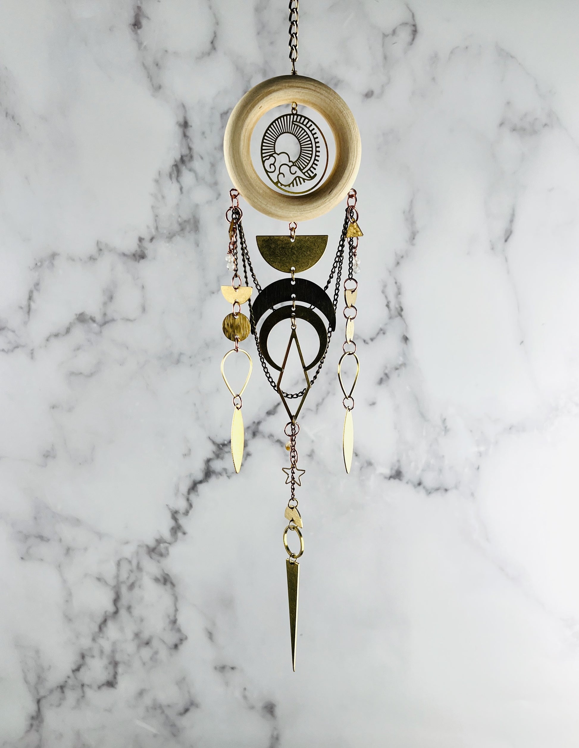 Decorative hanging ornament with geometric designs on a marble background. Sun & cloud charm with half circles, circles, crescent moons, diamonds, and triangles with wood ring. Handcrafted Moonstone and Citrine manifestation charm wall art created for intentional home decor and emotional balance.