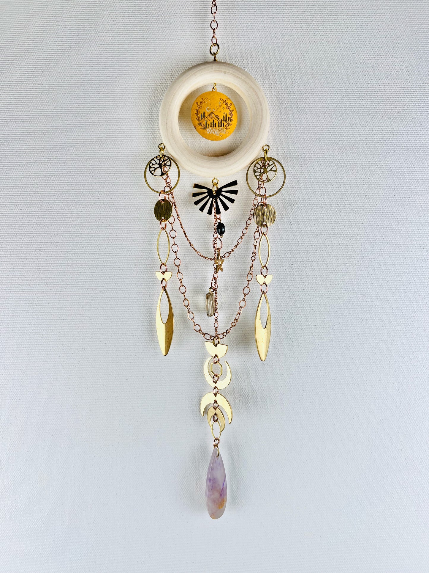 Decorative hanging crystal wall art with gold chain, stars, circles, eye shapes, crescent moons, rings, half circles, desert scene charm and tree of life. also has purple amethyst, black onyx and smoky quartz crystals with wood ring and on a light gray background