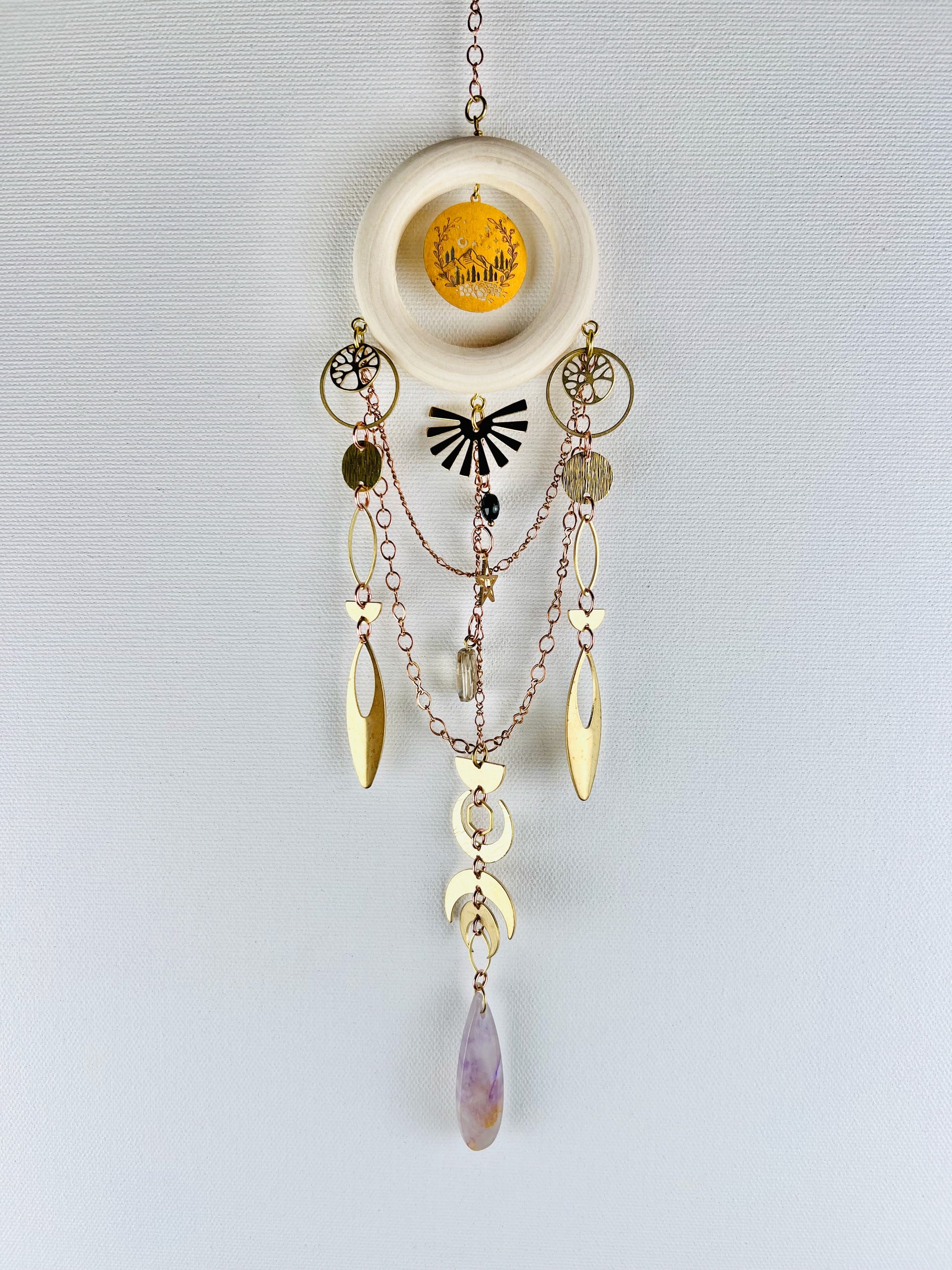 Decorative hanging crystal wall art with gold chain, stars, circles, eye shapes, crescent moons, rings, half circles, desert scene charm and tree of life. also has purple amethyst, black onyx and smoky quartz crystals with wood ring and on a light gray background