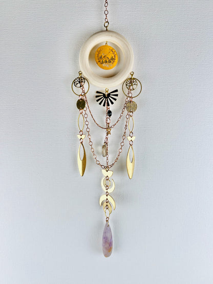 Decorative hanging crystal wall art with gold chain, stars, circles, eye shapes, crescent moons, rings, half circles, desert scene charm and tree of life. also has purple amethyst, black onyx and smoky quartz crystals with wood ring and on a light gray background