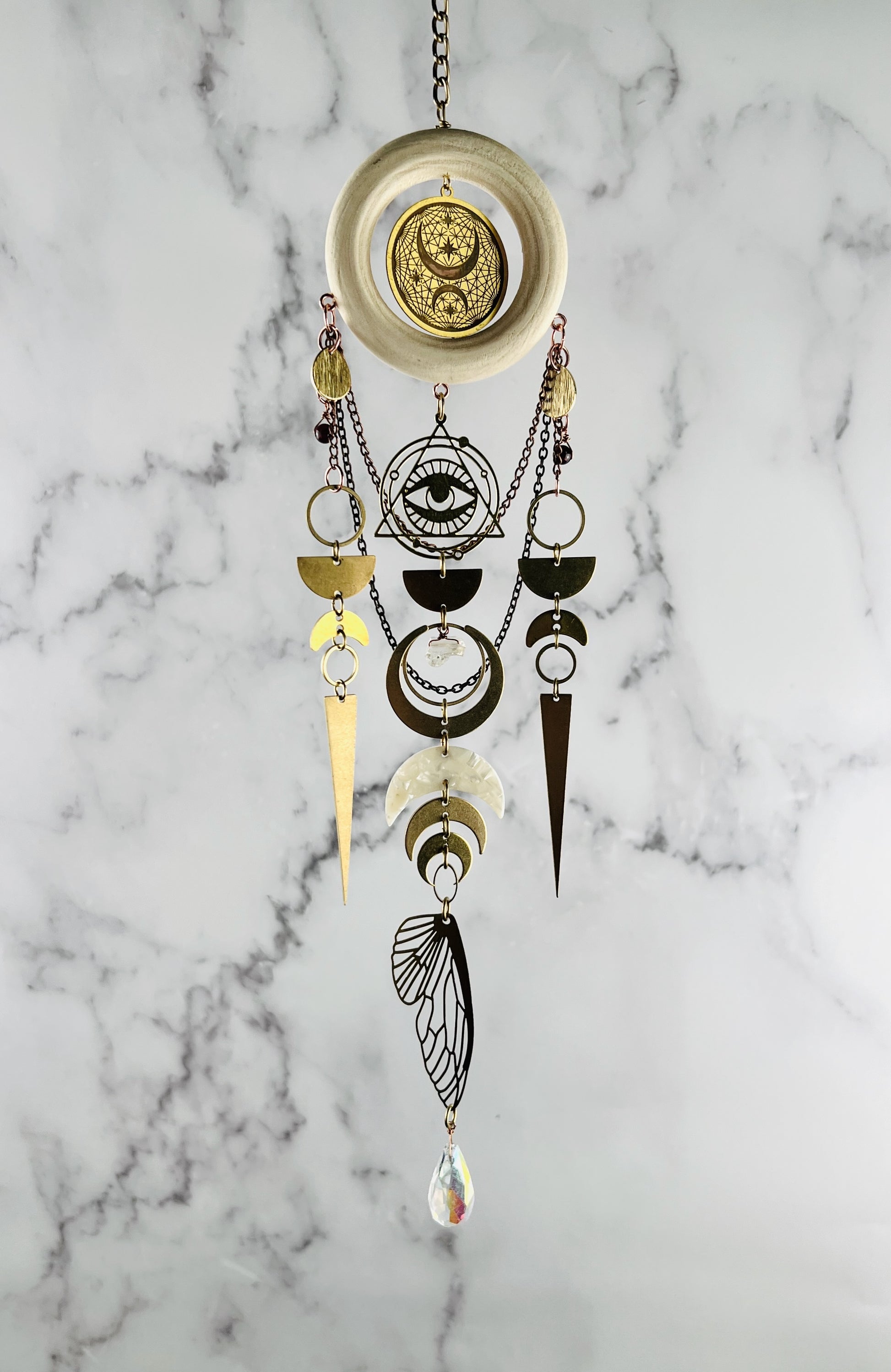 Hanging wall art with brass, silver, evil eye, geometric shapes, crescent moons crystals, chain and prism. Handcrafted Red Garnet and Citrine manifestation charm wall art created for intentional home decor and emotional balance.
