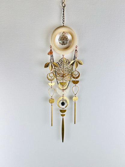 Decorative hanging suncatcher with prism, gold leaves, crescent moons, sunstone, drops, circles, chain and wood ring on a light gray background